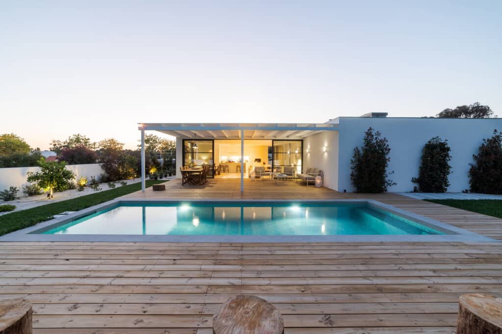 Maison Moderne avec Piscine et Terrasse en Bois Design Maison moderne avec piscine éclairée, grande terrasse en bois et pergola au crépuscule. Décoration extérieure épurée.