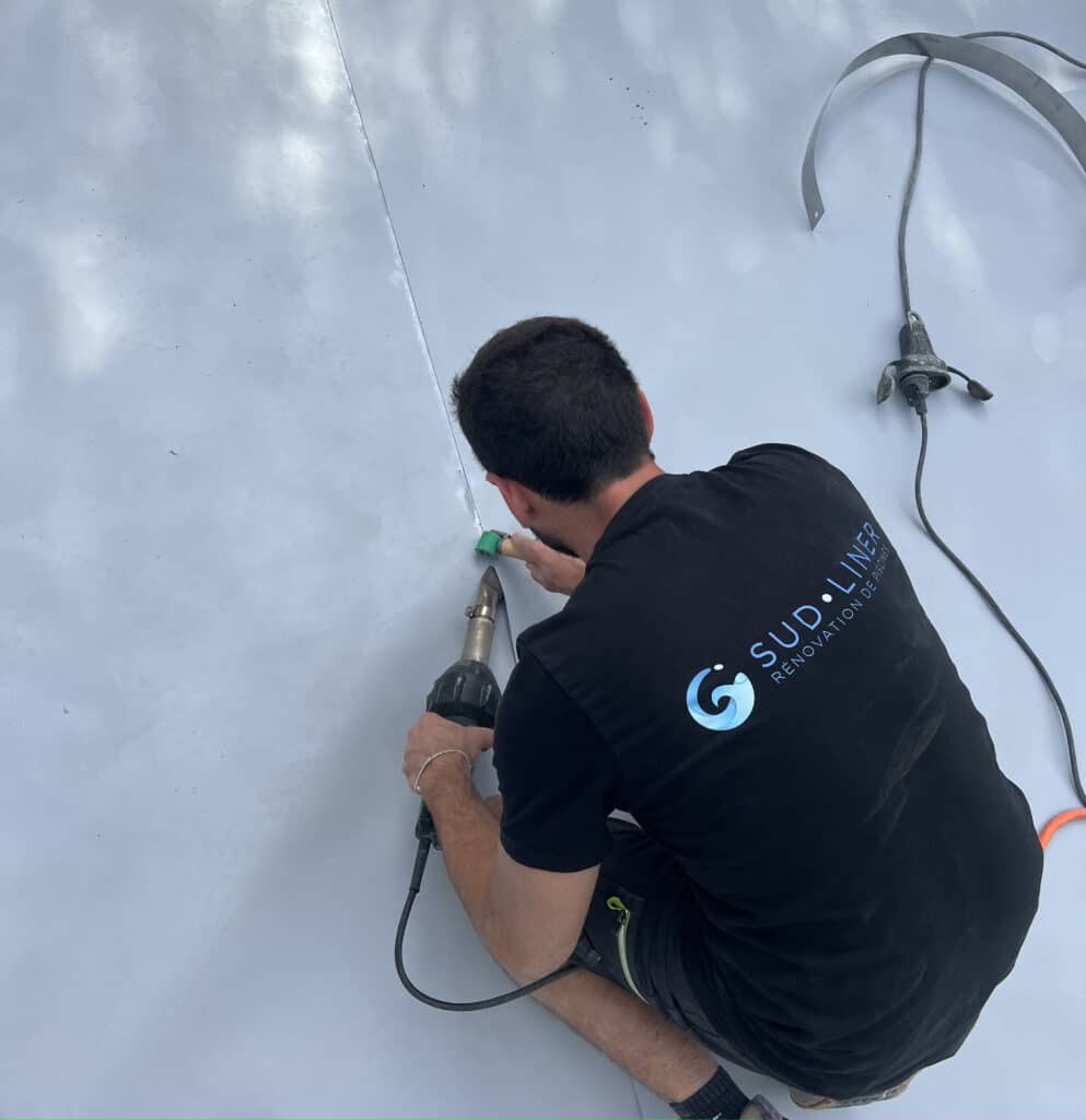 Pose de Liner de Piscine : Expertise Sud Liner en Rénovation Technicien de Sud Liner soudant un liner gris de piscine avec un pistolet thermique et un rouleau de pression.