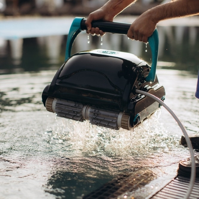 Robot de piscine : un nettoyage efficace et automatique Nettoyeur de piscine robotisé noir et turquoise soulevé hors de l'eau, évacuant l'eau après un cycle de nettoyage.