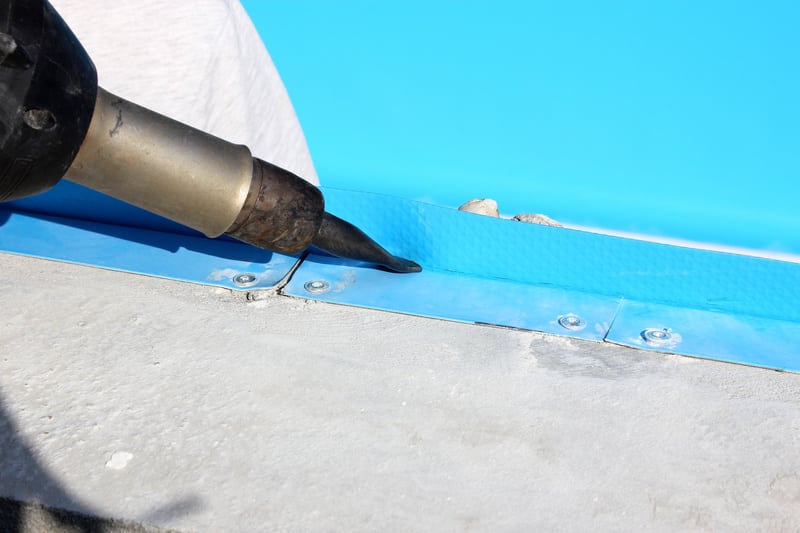 Pose de liner PVC : soudure thermique pour piscine Soudage à air chaud d'un liner de piscine bleu sur une bande métallique fixée au rebord en béton.