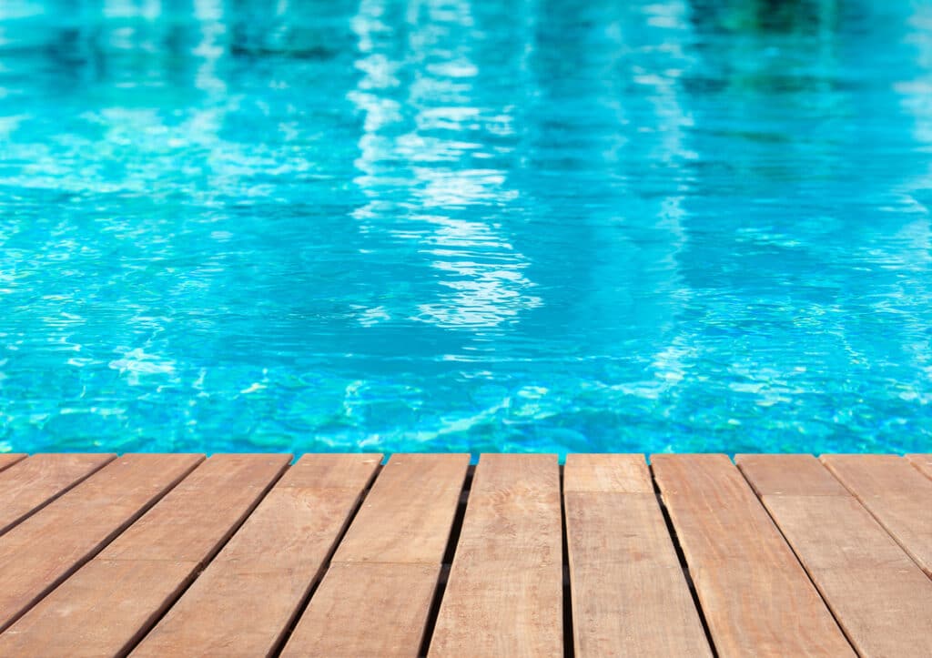 Terrasse en bois au bord d'une piscine bleue turquoise Terrasse en bois clair au bord d'une piscine à l'eau bleue turquoise scintillante, évoquant la détente en plein air.