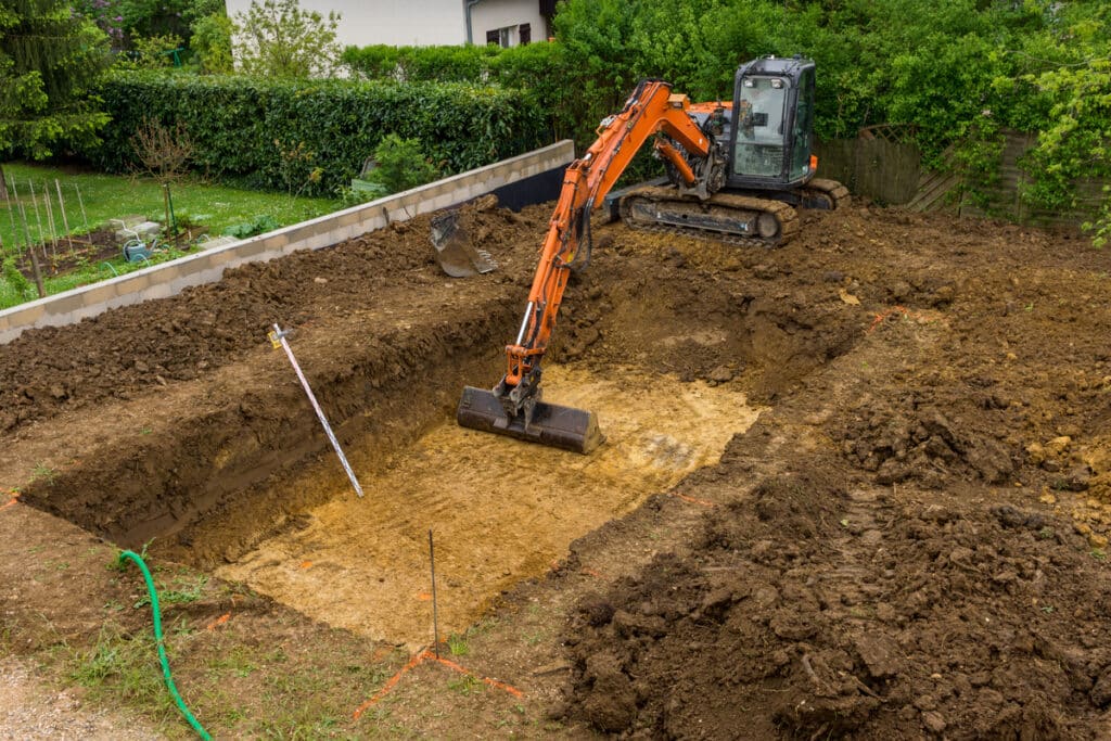 Terrassement de Jardin : Excavatrice Creusant une Piscine Excavatrice orange creusant une fosse pour une piscine dans un jardin lors de travaux de terrassement.